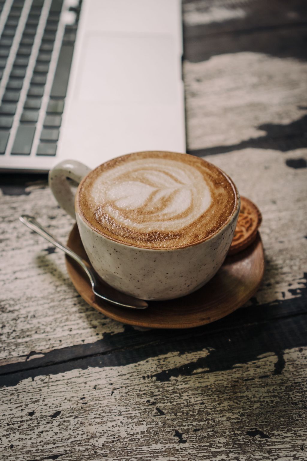 A latte with decorative foam next to a laptop